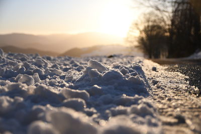 Close-up of snow on land against sky during sunset