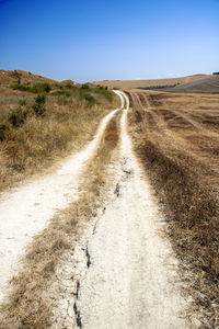 Dirt road passing through landscape against clear sky