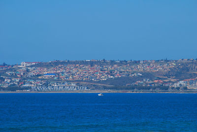Aerial view of townscape by sea against clear blue sky