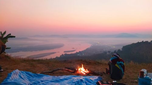 Man sitting on shore against sky during sunset
