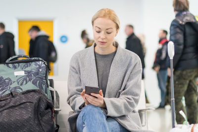 Woman using smart phone sitting at airport