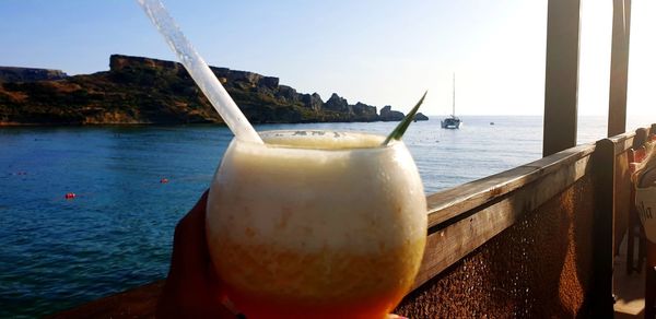 Close-up of drink on sea against sky