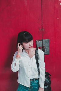 Young woman wearing red dress standing against wall