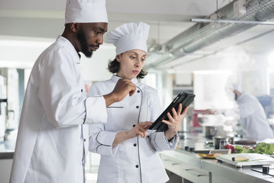 Chef sharing digital tablet with colleague standing in restaurant kitchen