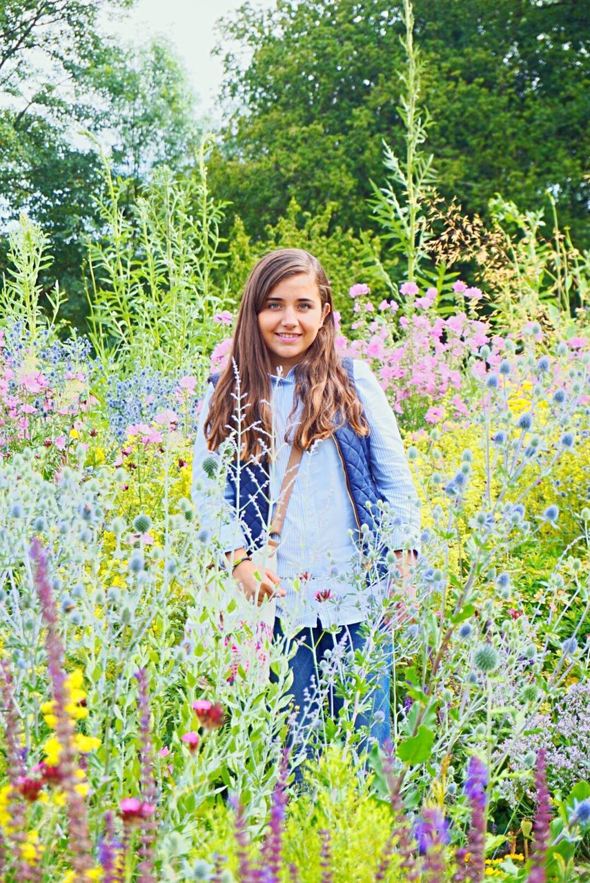 person, young adult, lifestyles, looking at camera, young women, smiling, leisure activity, portrait, casual clothing, front view, flower, standing, long hair, tree, plant, happiness, growth