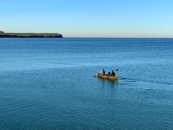 People rowing boat in sea against clear sky
