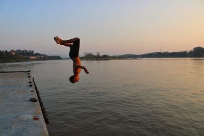 Man jumping in lake against sky during sunset