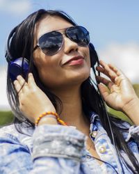 Smiling woman listening music through headphones against sky