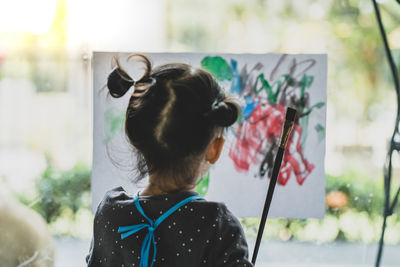 Rear view of girl painting on paper