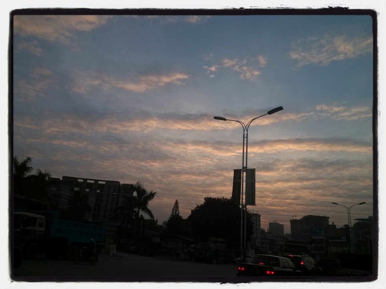 building exterior, architecture, transfer print, built structure, sky, city, cloud - sky, car, auto post production filter, sunset, land vehicle, street light, transportation, cloudy, street, cloud, dusk, city life, mode of transport, silhouette