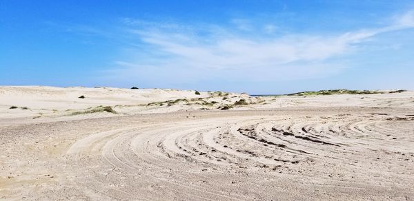 Tire tracks on desert road against sky