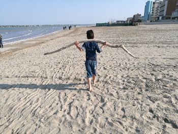Rear view of boy on beach against clear sky