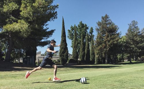 Full length of man kicking soccer ball at park