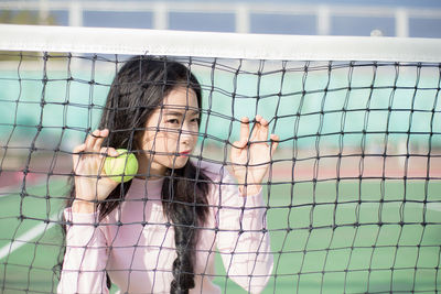 Young woman holding ball while standing against net on court