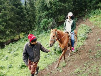 Rear view of woman riding horse standing on field