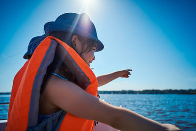 Side view of girl wearing life jacket standing in boat on sea