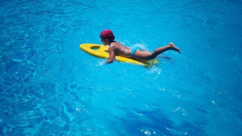 High angle view of shirtless boy swimming on surfboard in pool