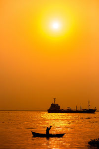 Silhouette people on sea against orange sky