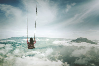 Woman swinging over cloudscape against sky