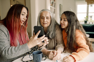 Woman with dyed hair showing smart phone to mother and daughter at home