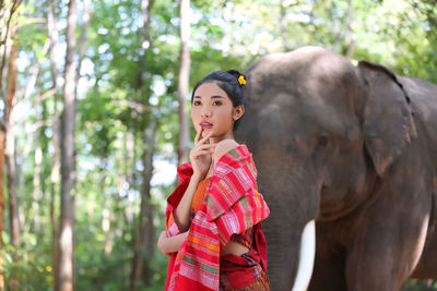 Thoughtful woman looking away while standing against elephant