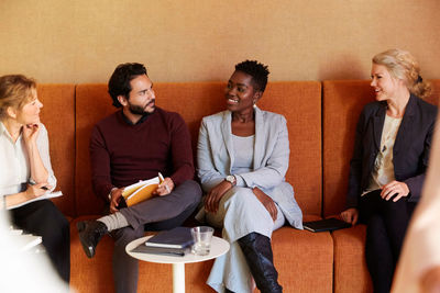 Smiling male and female entrepreneurs sitting with coworkers on sofa at workplace