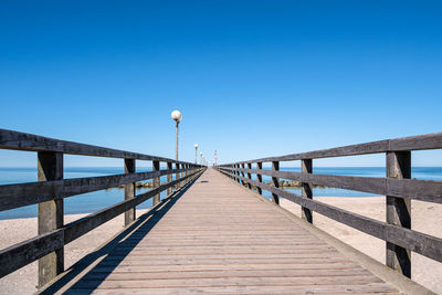 Footbridge over pier against clear blue sky