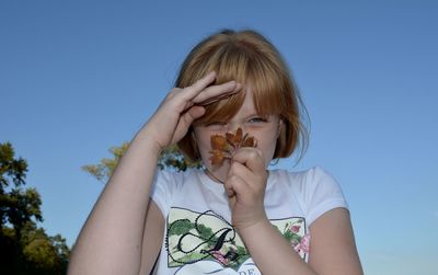 Portrait of girl holding flowers against clear blue sky