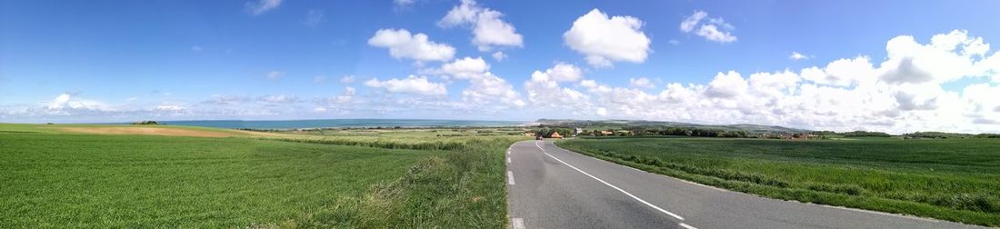 Panoramic view of road amidst field against sky