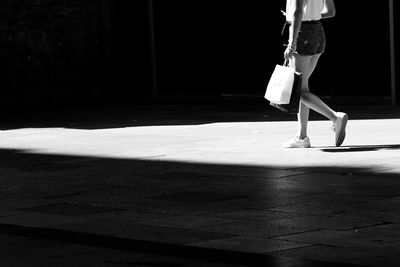 Low section of woman walking on footpath during sunny day