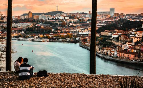 Rear view of man sitting by cityscape against sky