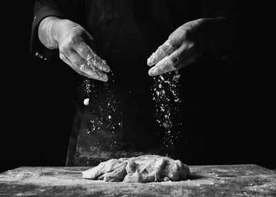 Midsection of chef preparing food against black background