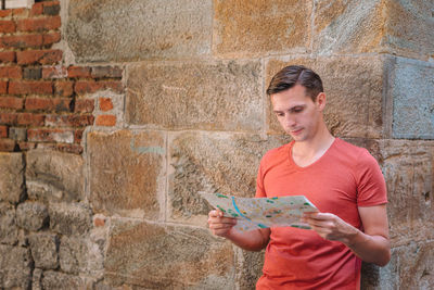 Side view of young man using mobile phone against wall