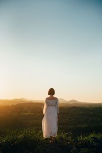 Rear view of woman standing on field against clear sky during sunset