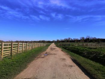 Road amidst field against blue sky