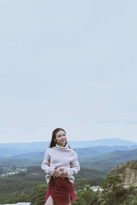 Portrait of young woman standing against sky