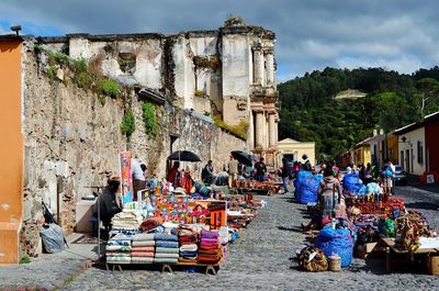 People at market amidst houses against cloudy sky