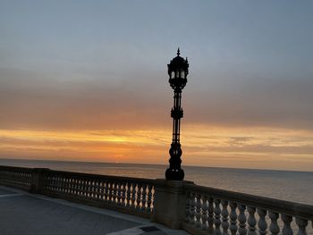 Street light by sea against sky during sunset