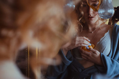 Midsection of young woman holding orange while standing by mirror at home