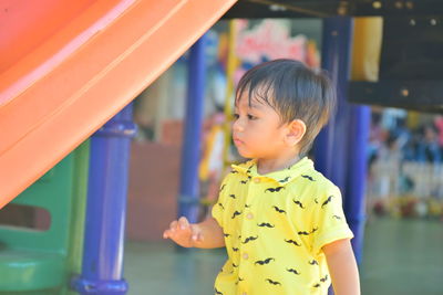 Cute boy looking away while standing by slide in playground