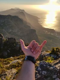 Close-up of human hand gesturing horn sign on rock during sunset