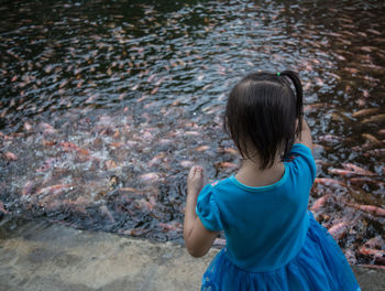 Rear view of girl standing against fish swimming in lake