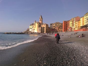 People walking on beach by buildings against sky in city