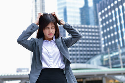 Young woman looking away while standing against buildings in city