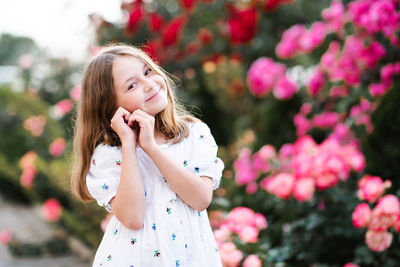 Happy smiling cheerful little child girl 6-7 year old show heart with fingers pose over rose flower