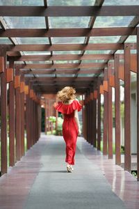 Rear view of woman wearing red dress while walking in corridor