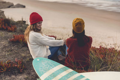 Women sitting by surfboard at beach