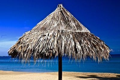 Thatched roof parasol on shore against blue sky