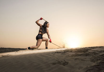 Young woman jumping on sand against sky
