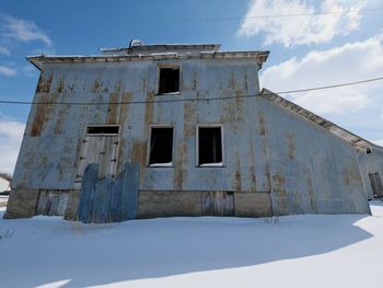 Low angle view of snow covered abandoned building against sky